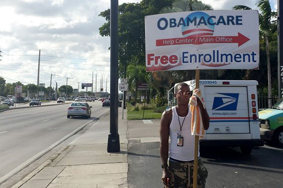 Henry Bowles, an uninsured man in Fort Lauderdale, Fla., holds a sign directing people to an office that helps people enroll in health law insurance coverage. (Photo by Phil Galewitz/KHN)