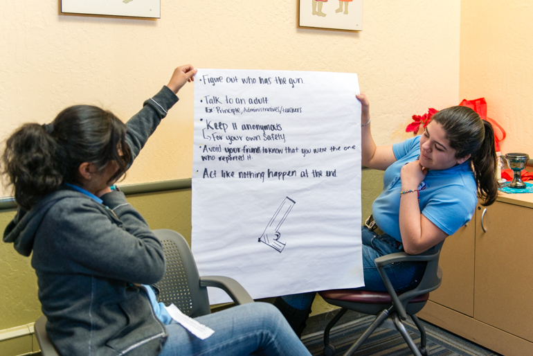 Graciela Pérez, de 17 años, y Nayely Espinoza, de 17, sostienen su asignación grupal durante una presentación en clase. Los estudiantes se preparan para sus prácticas de salud mental (Heidi de Marco/KHN)