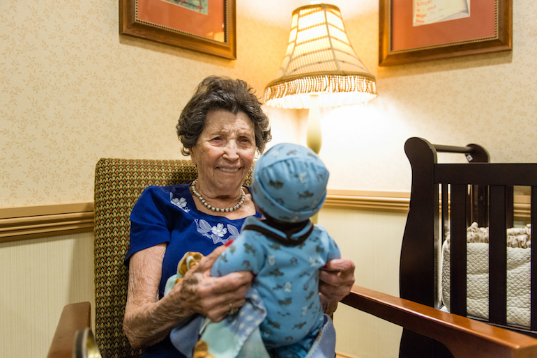 Vivian Guzofsky, 88, holds a baby at Sunrise Senior Living in Beverly Hills, California, on August 2, 2016. Some nursing homes are using a technique called doll therapy to ease anxiety among their residents with dementia.  (Heidi de Marco/KHN)