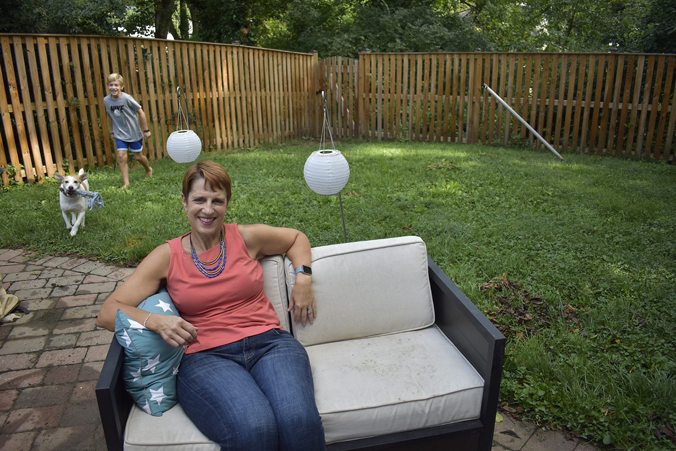 Angie Melton sits in her yard with son and dog playing outside