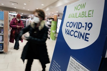 Shoppers at a pharmacy walk past a sign advertising covid vaccines.