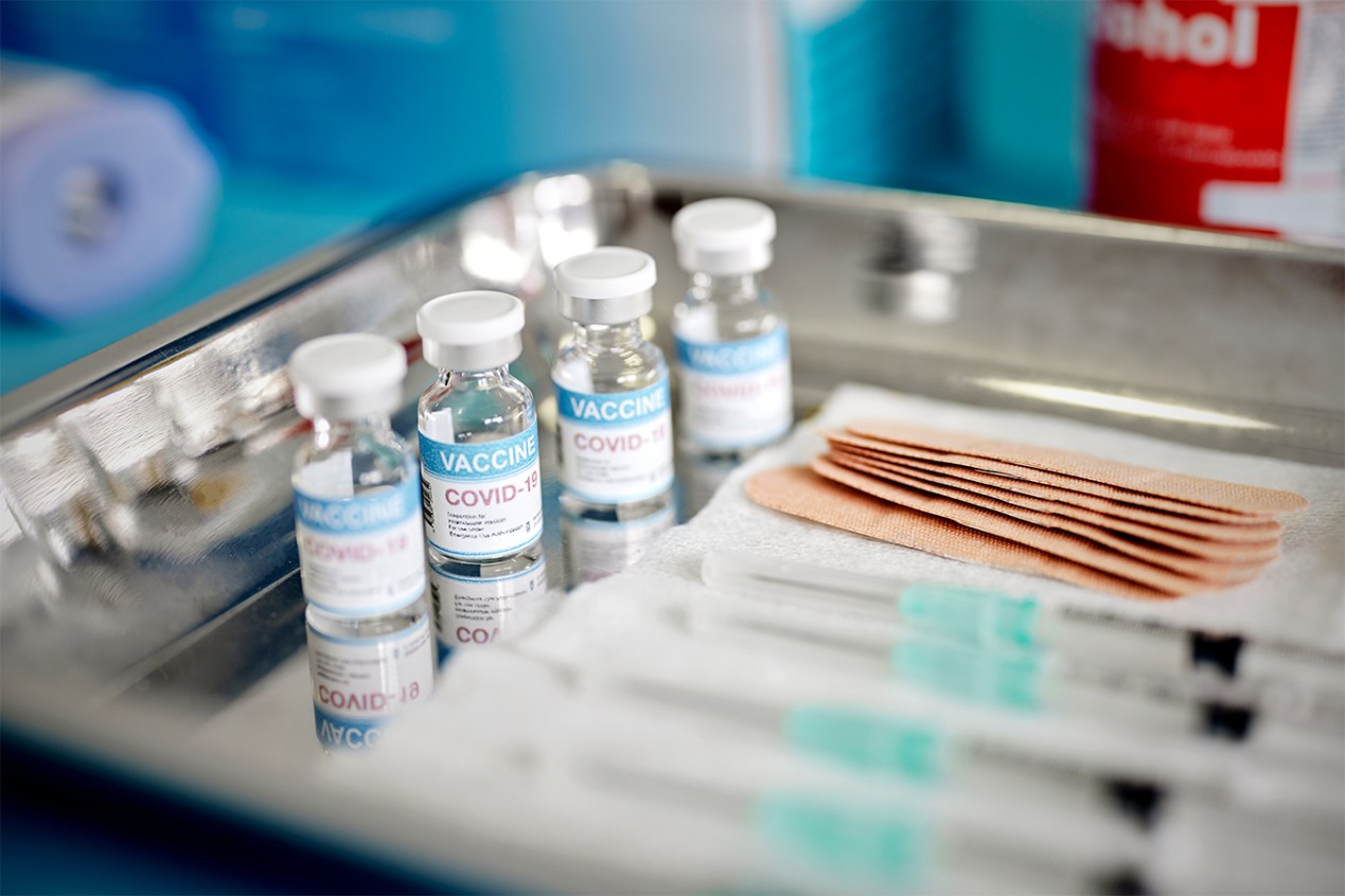 Vials of covid vaccine and syringes are arranged on a metal tray.