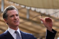 Gov. Gavin Newsom raises his right hand while talking to reporters at a press conference.