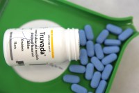 A bottle of Truvada, an HIV prevention drug, tips out blue pills onto a pill counting tray.