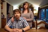 Sean Deines sits at a table in his home with his wife, Rebekah, standing behind him with her hands on his shoulders.