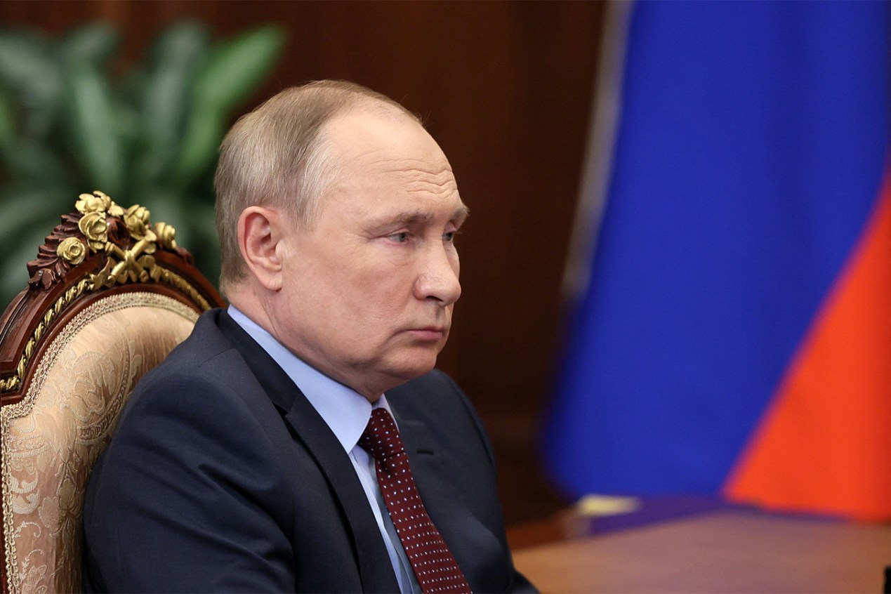 Vladimir Putin is seen sitting in a chair, looking across a table.