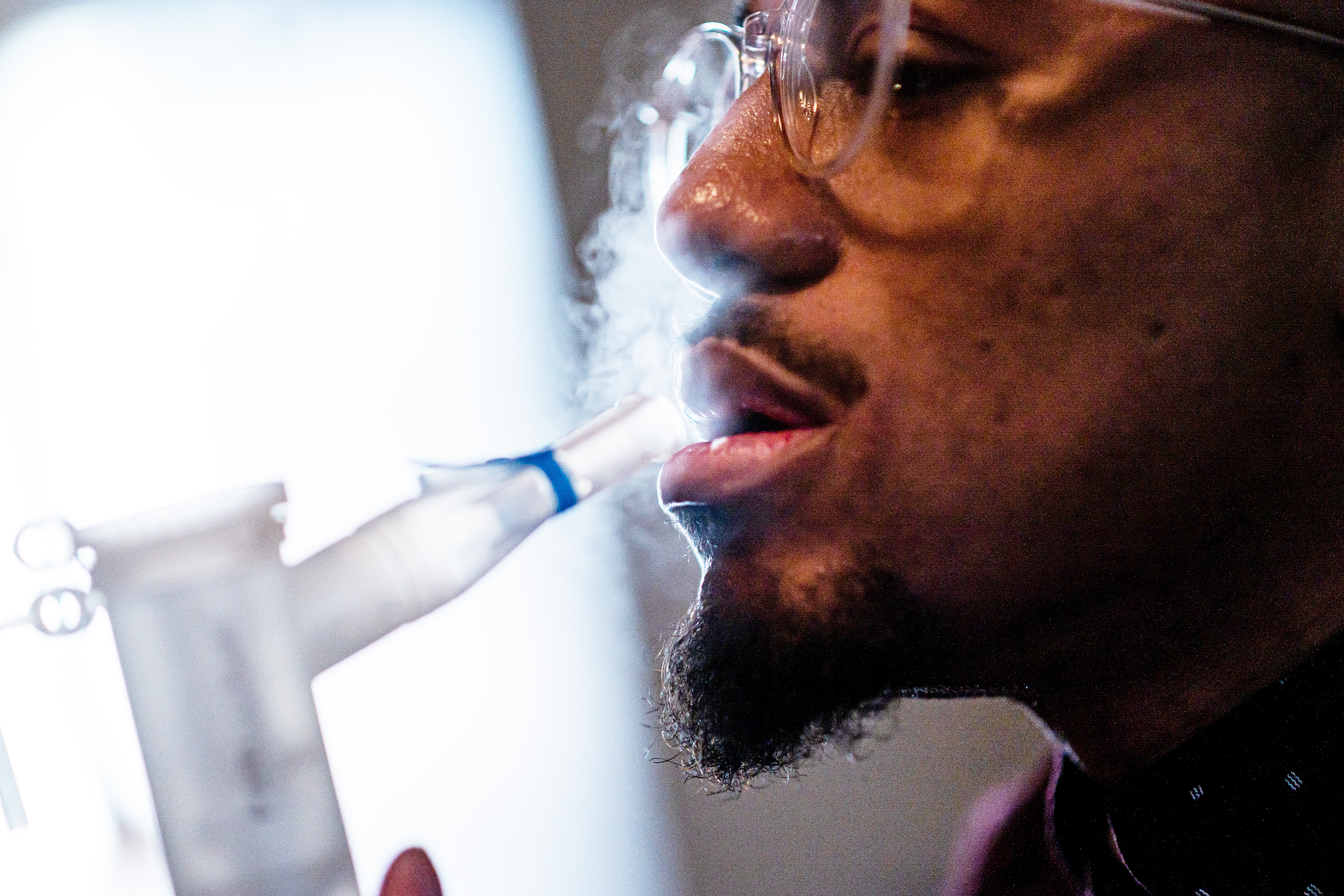 A nebulizer aerosolizes medication that Nicholas Kelly, seen in profile on the right, breathes in through a mouthpiece. A window is seen in the background, casting dramatic shadows.