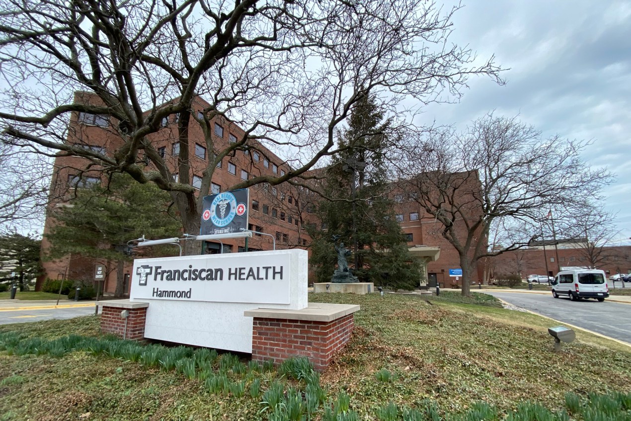 A sign outside of a hosp ital reads, "Franciscan Health Hammond." The hospital is seen in the background behind trees.