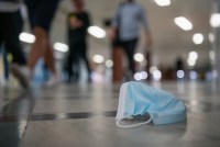 A surgical mask on the floor as many people walk past it.