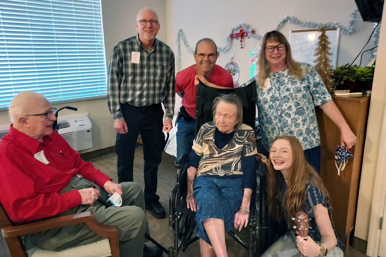 A group of family members surround Jean White's mother, who sits in a wheelchair. They are posing for a family photo.
