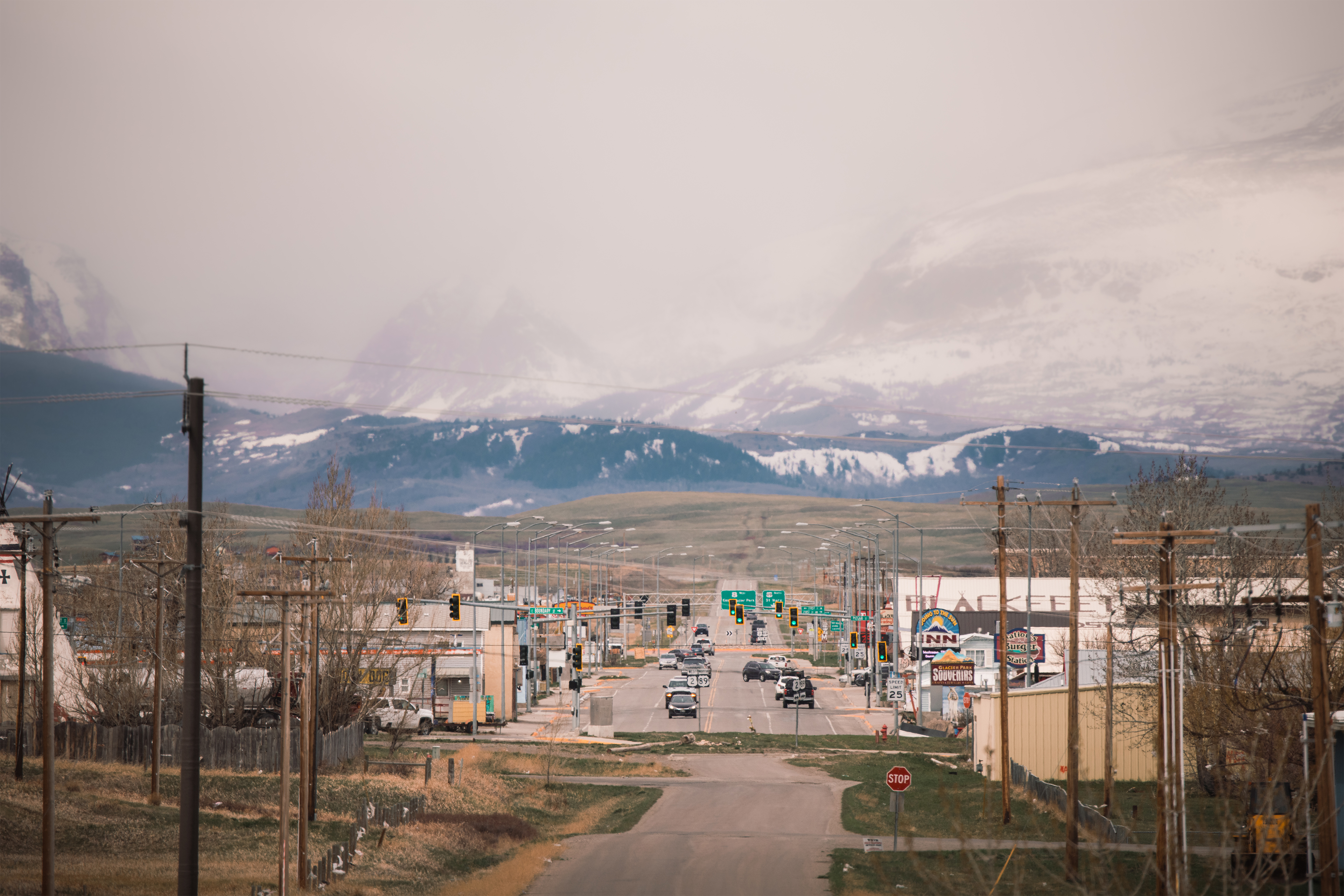 Foto lanskap menunjukkan sebuah jalan di Browning, Montana dengan pegunungan menjulang di belakangnya sebagai latar belakang.