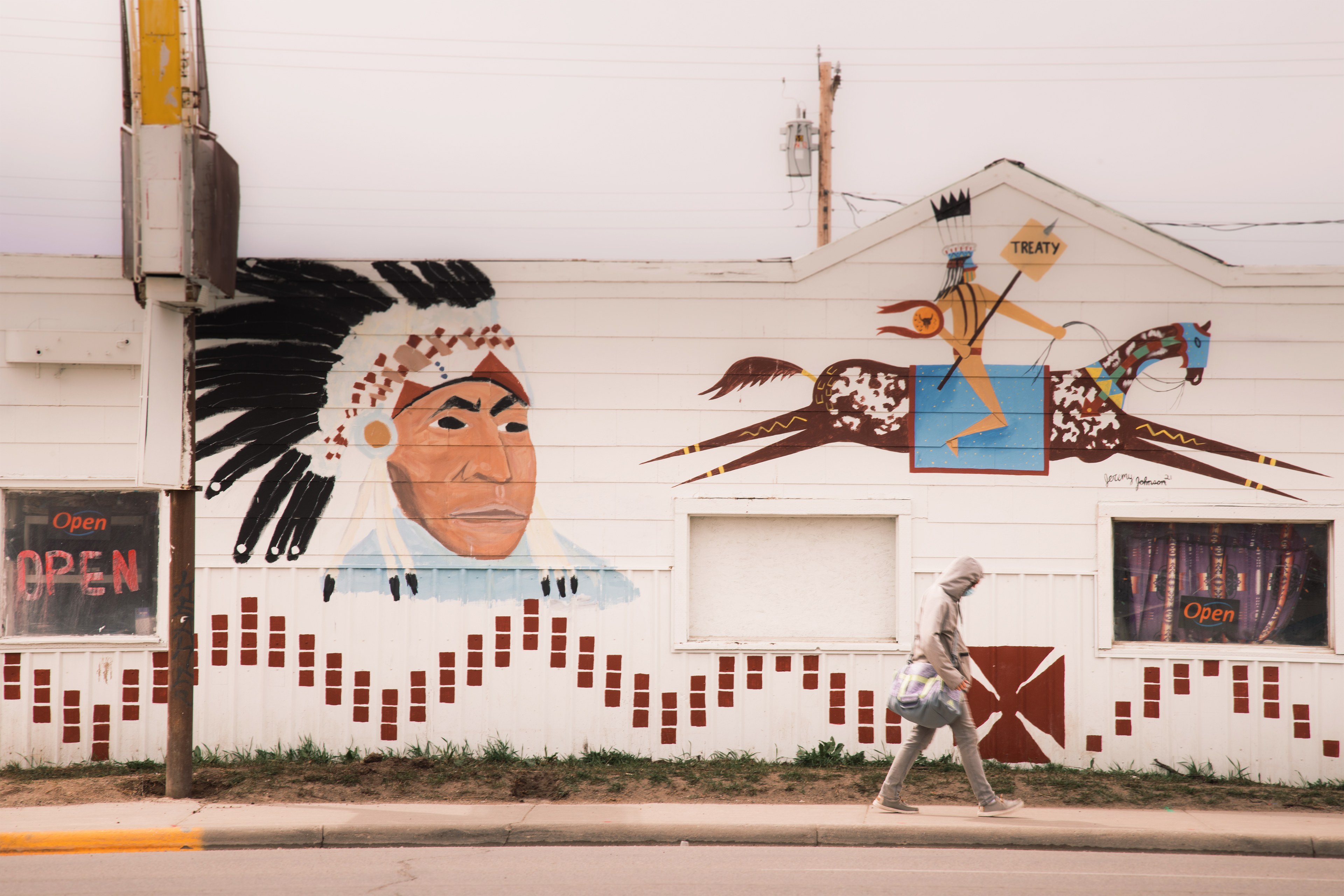 Seseorang terlihat berjalan di trotoar dekat sebuah bangunan di Browning, Montana.  Sisi bangunan dicat dengan gambar seorang pria asli Amerika yang mengenakan topi perang.  Lukisan lain menunjukkan seorang penduduk asli Amerika yang sedang menunggang kuda memegang tombak yang menembus sebuah tanda yang berbunyi, "PERJANJIAN."