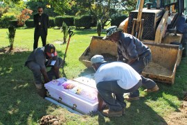 Three cemetery workers lower a pink casket with an image of Calyia Stringer printed on it into a plot in the ground.