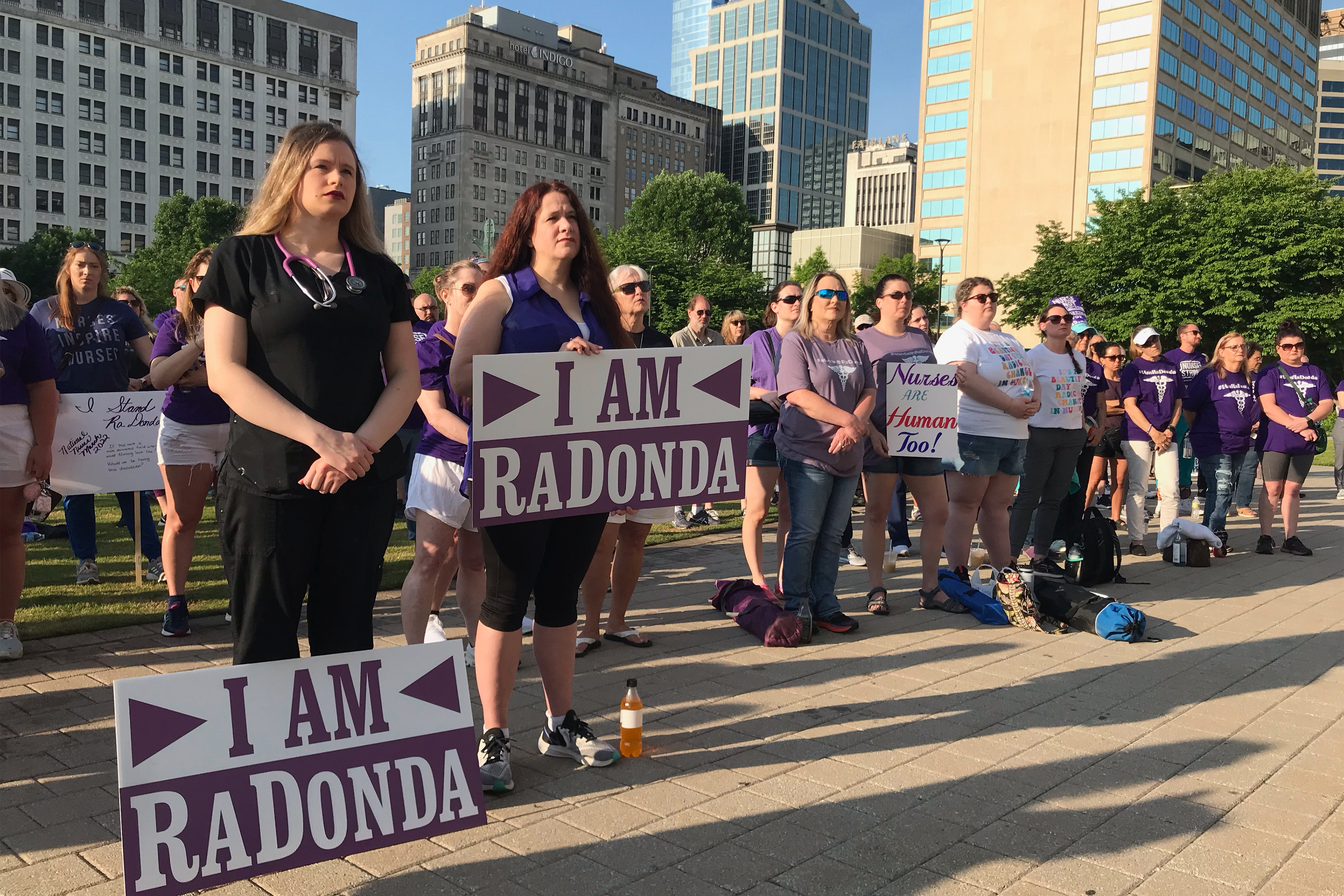 A crowd of protesters is seen holding signs which read, "I am Radonda." Most of the crowd is wearing purple clothes.
