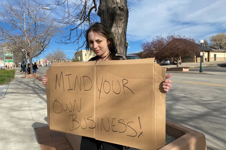 A young woman holds a sign that reads, "Mind Your Own Business!"