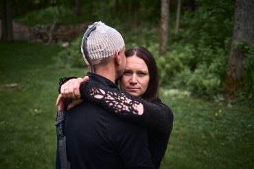 A woman looks at the camera while she hugs her husband.