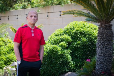 A photo shows Danilo Manimtim standing outside in front of green bushes.