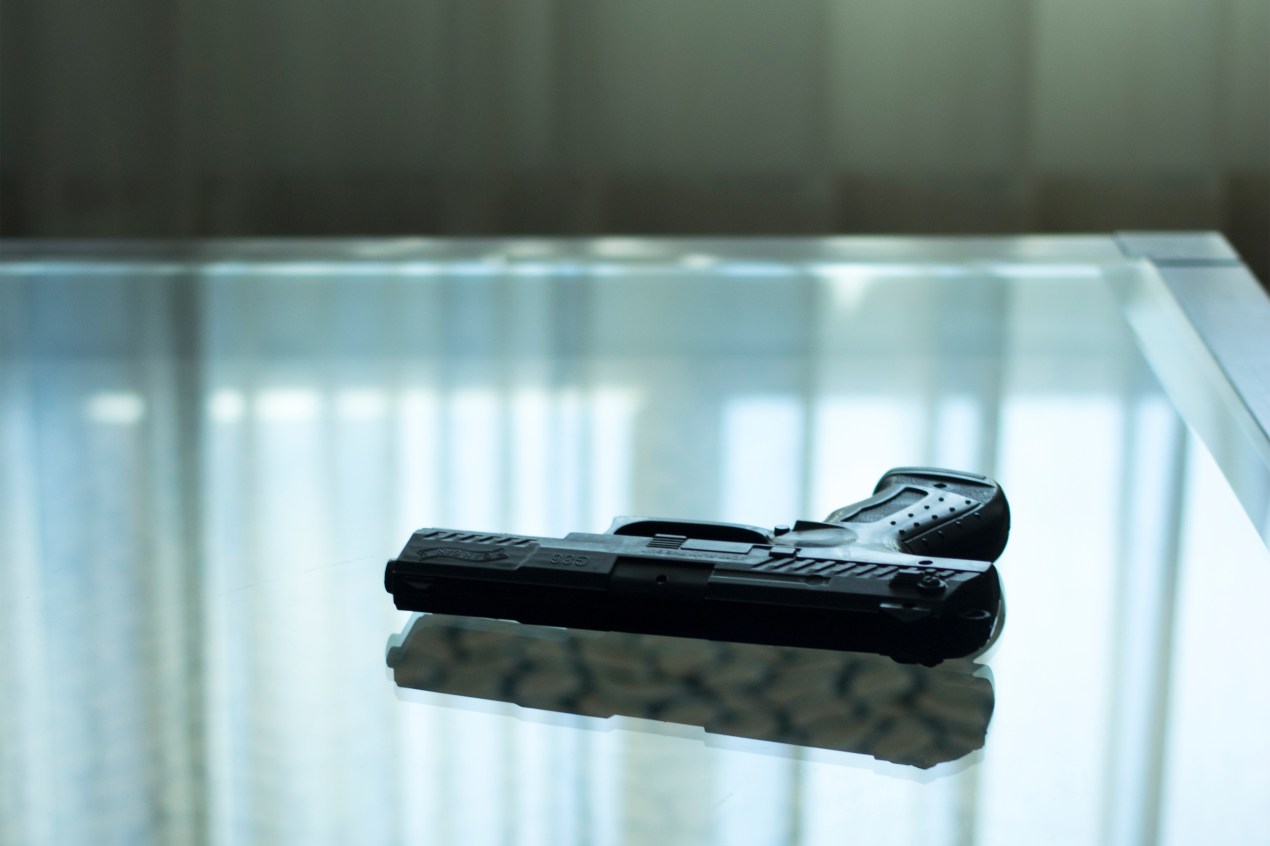 A photo shows a gun resting on a glass table.