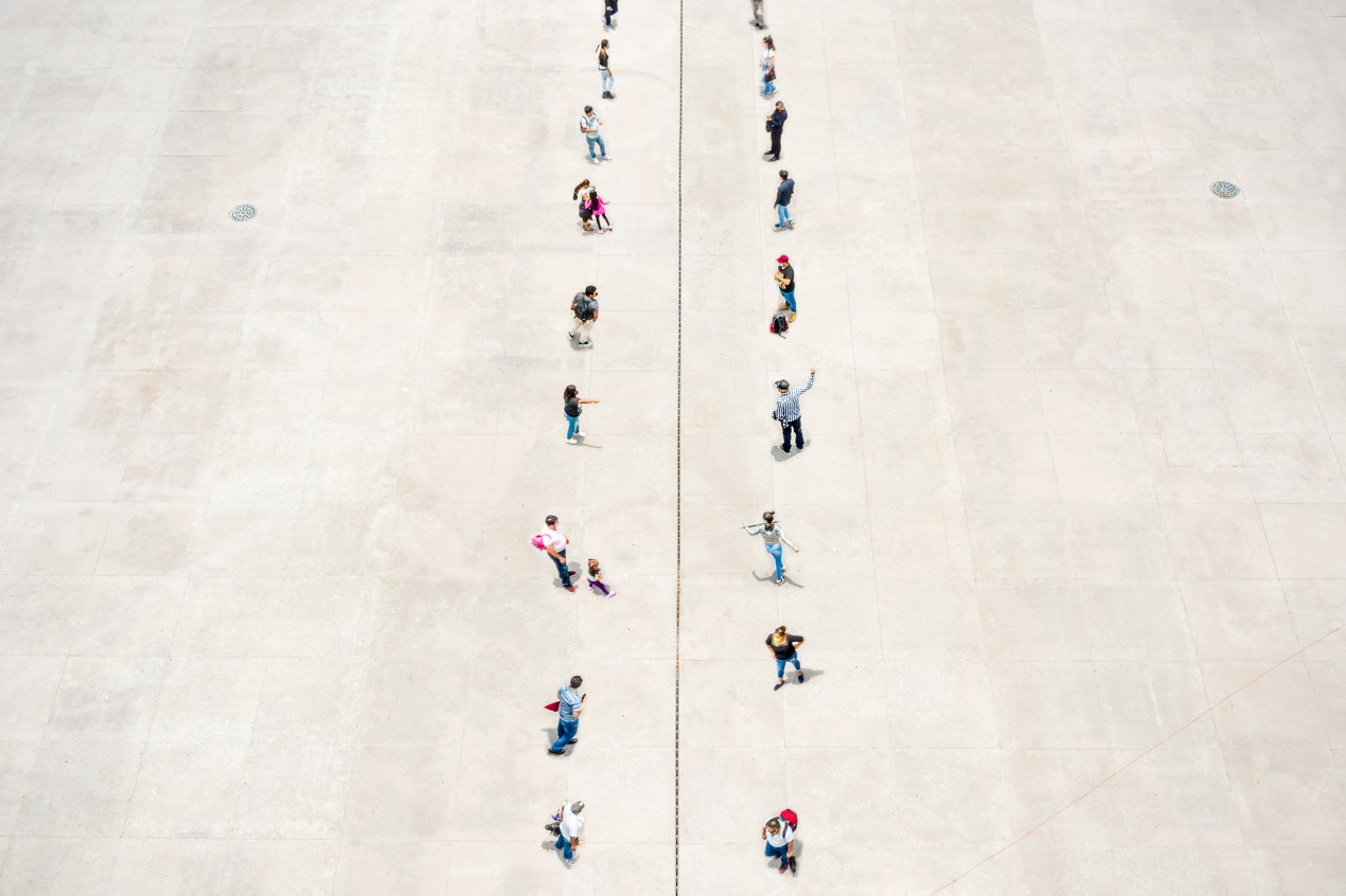 A photo illustration shows two rows of people standing on separated zones, divided in the middle with a dashed line.