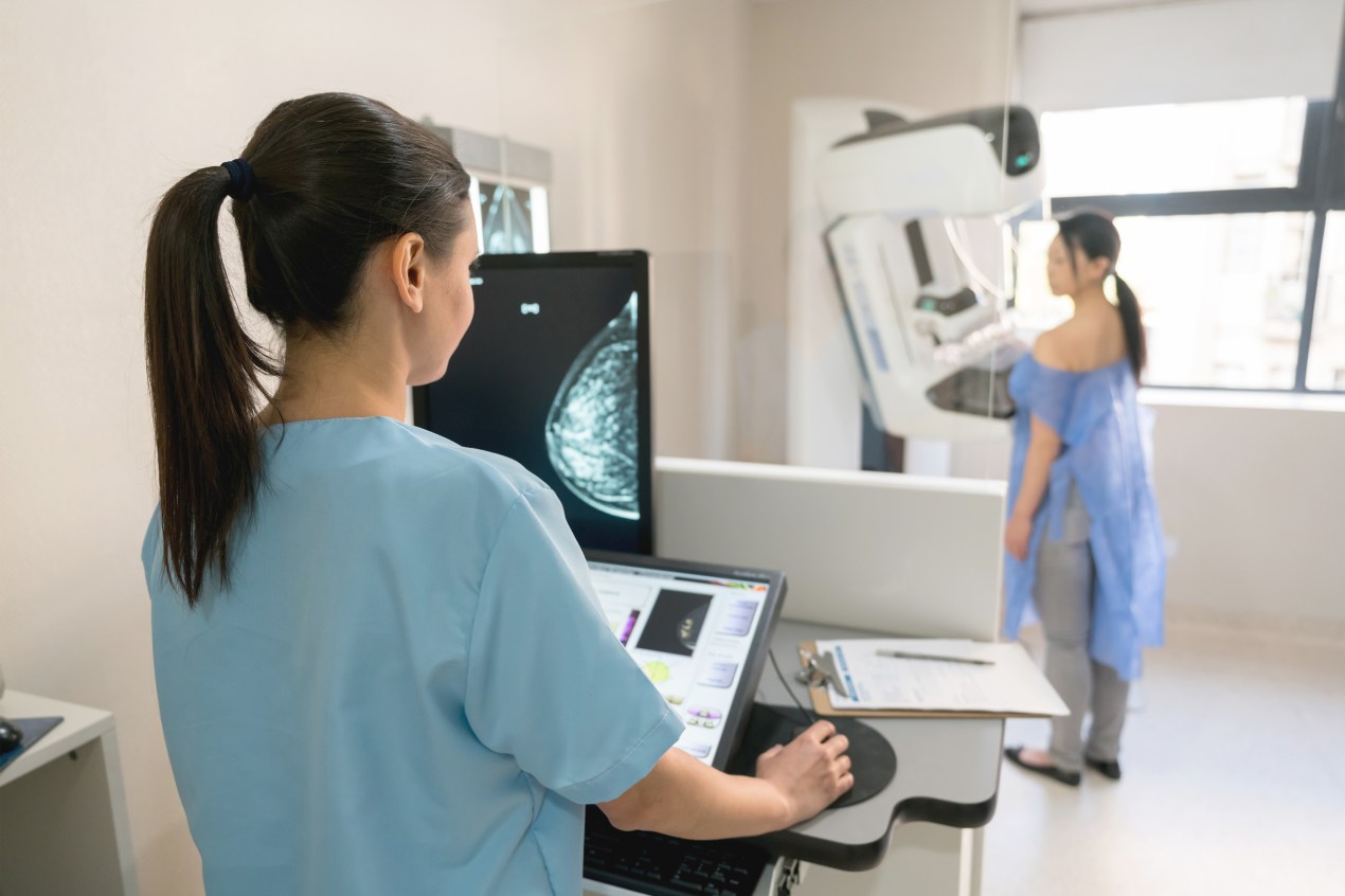 A nurse is seen from behind administering a mammogram to a woman.