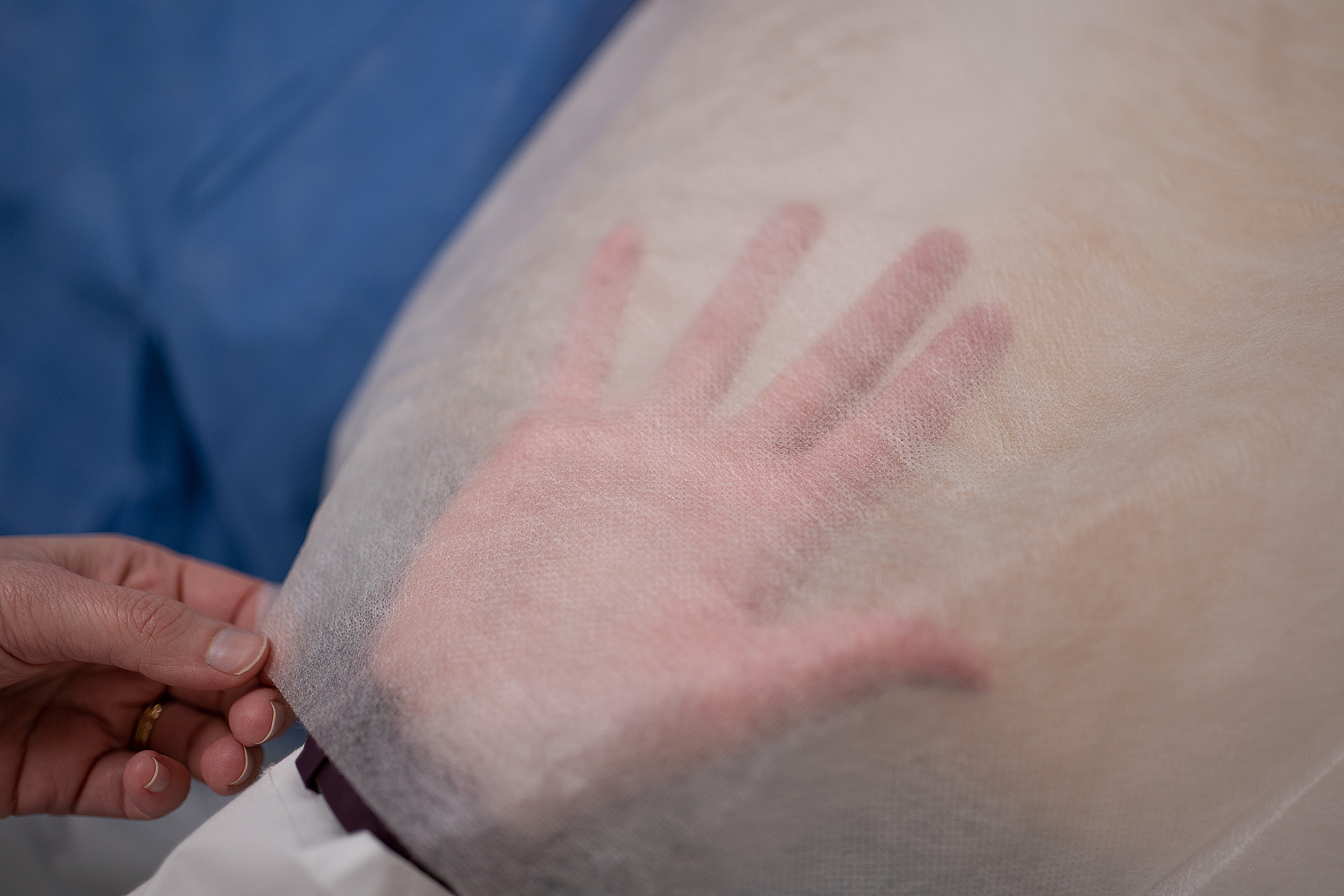 A close up photo shows Karen Haberland's hand visible under the shear fabric of a medical isolation gown.