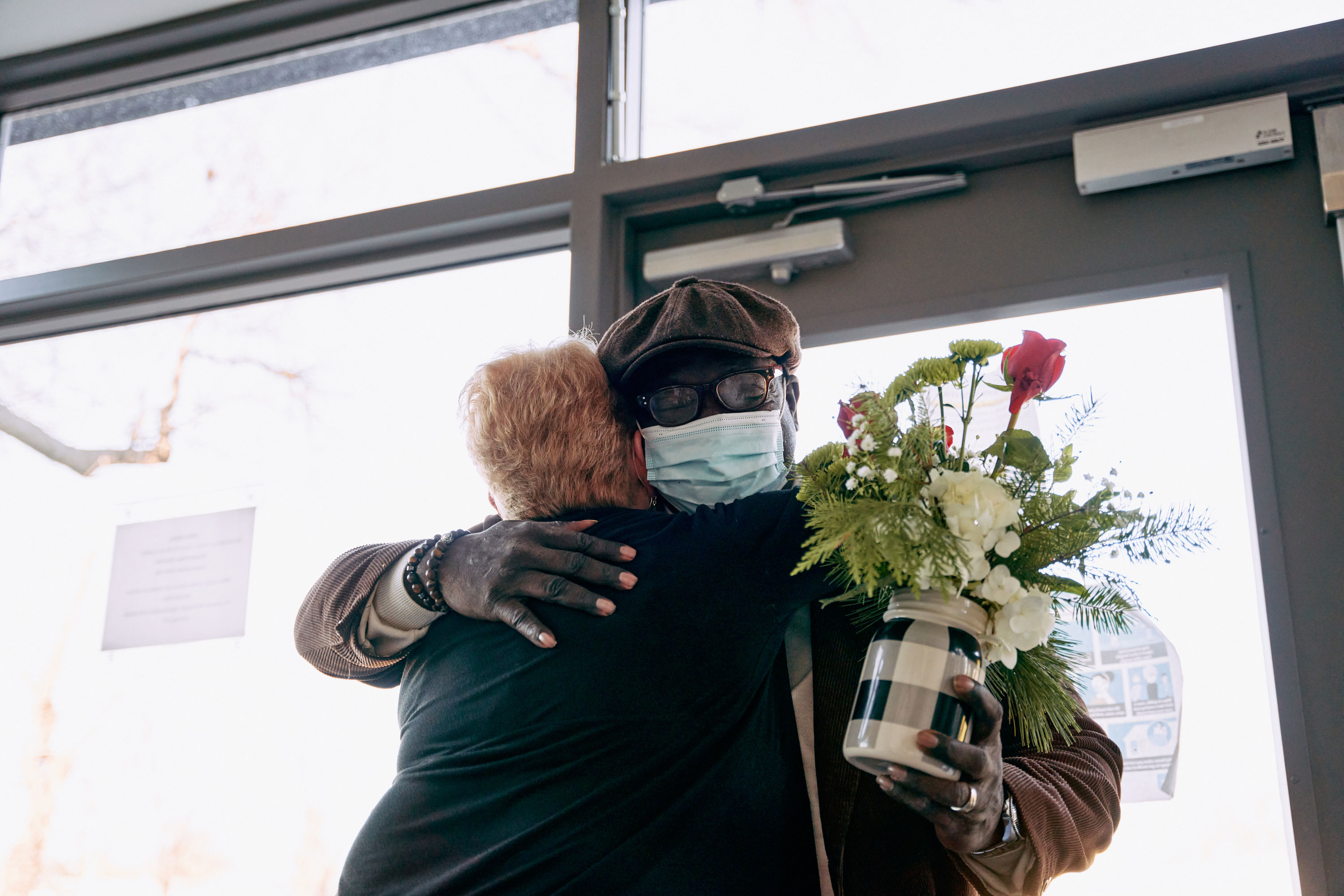 A man carrying a bouquet of flowers hugs a woman.