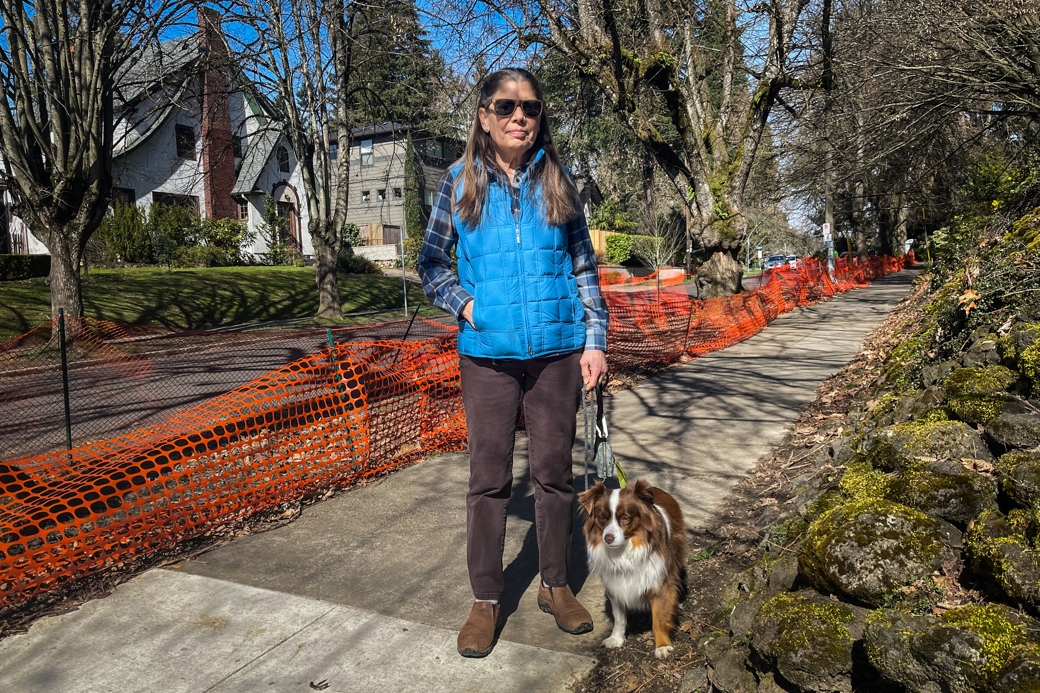 A photo shows TJ Browning with her dog on the sidewalk near her home. Orange fencing lines the edge of street.