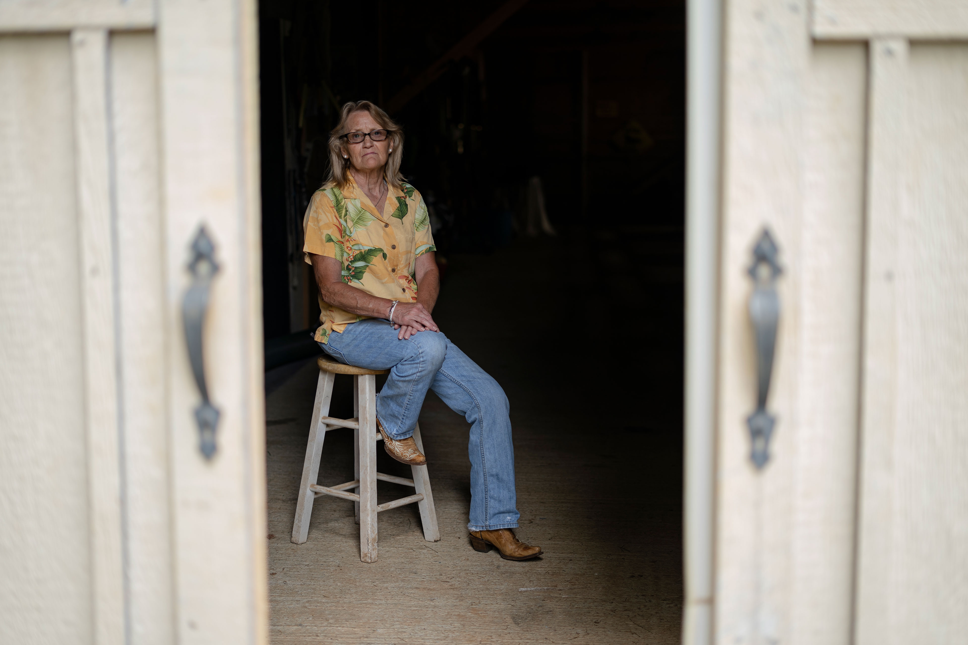 A woman sits on a stool in a barn.