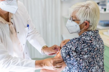 A photo shows a doctor putting a bandage on an elderly patient's arm after she gets vaccinated.