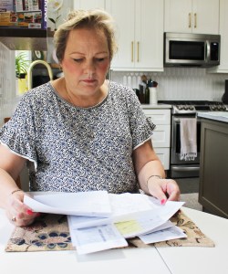 A photo shows Peggy Dula in her kitchen looking at her medical bills.