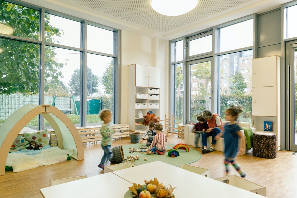 a group of young children play in a brightly lit room surrounded by windows at a daycare center