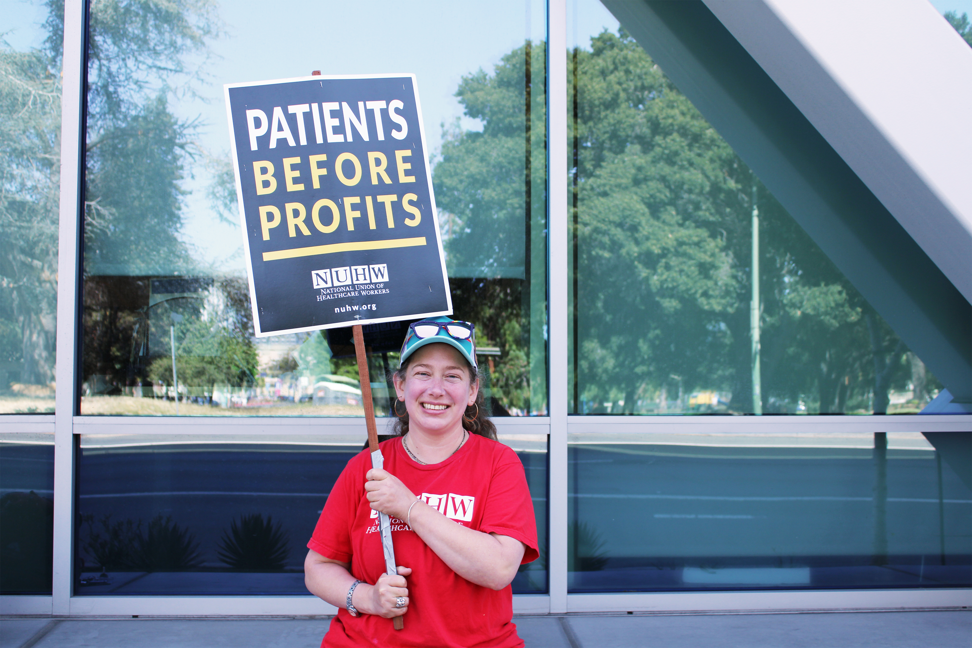 A photo shows Alicia Moore standing outside of the Kaiser Permanente hospital in Oakland, California. She is holding a sign that reads, "Patients before profits."