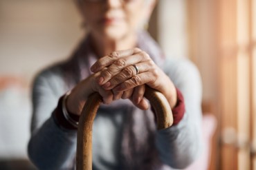 A photo shows an elderly woman sitting with her hands resting on top of her cane.