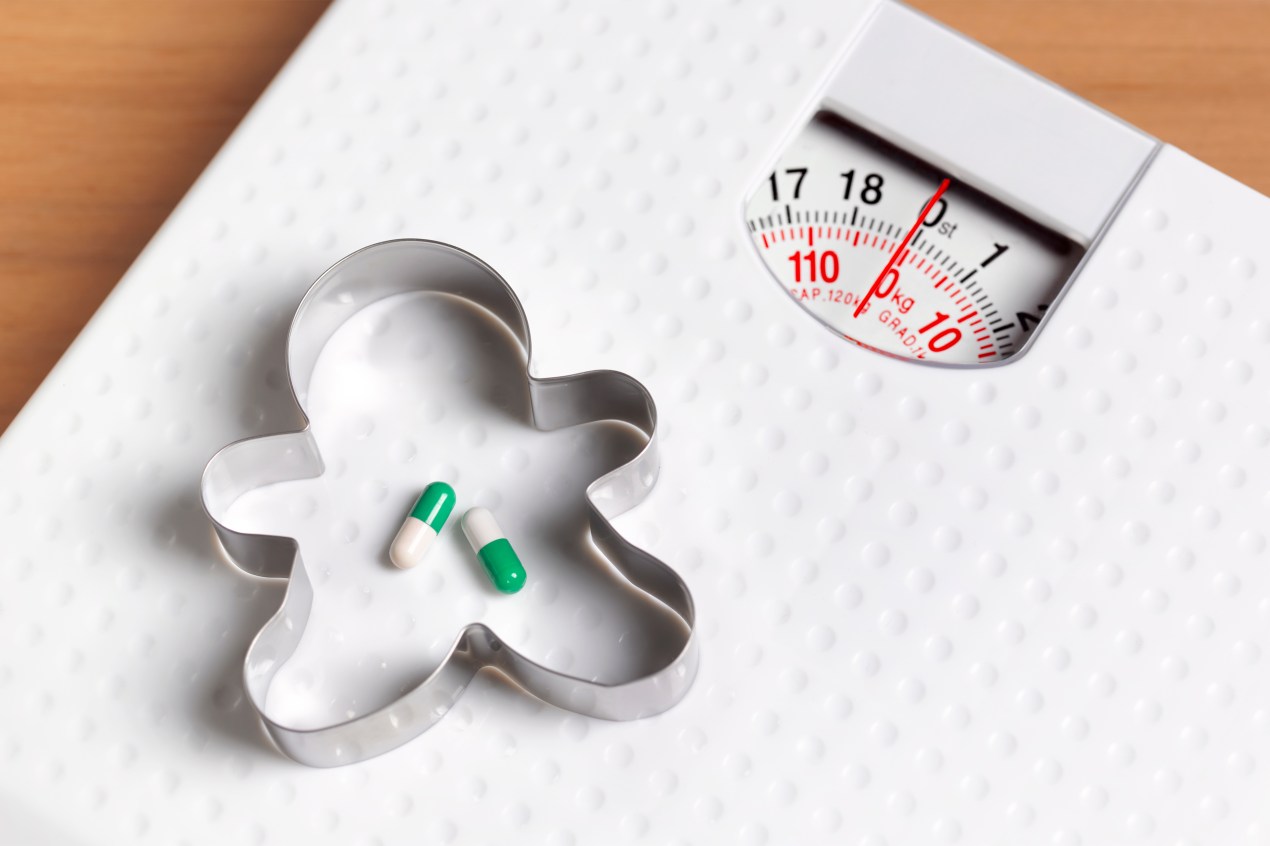 A photo shows pills on a bathroom scale surrounded by a human-shaped cookie cutter, suggesting weight loss.