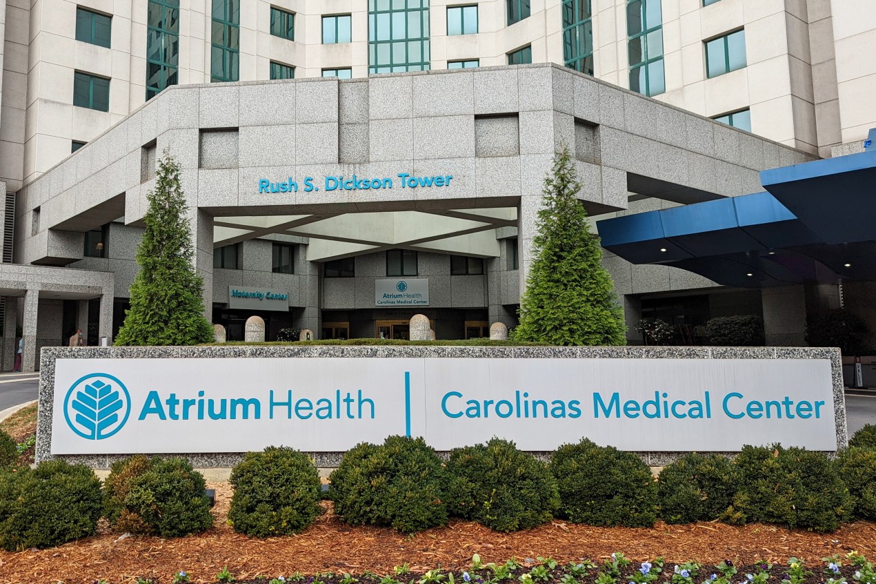 A photo shows an exterior of Carolinas Medical Center. A large sign in front of the building bears the name of the hospital and Atrium Health, its owner.