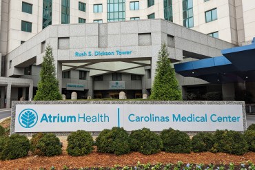 A photo shows an exterior of Carolinas Medical Center. A large sign in front of the building bears the name of the hospital and Atrium Health, its owner.