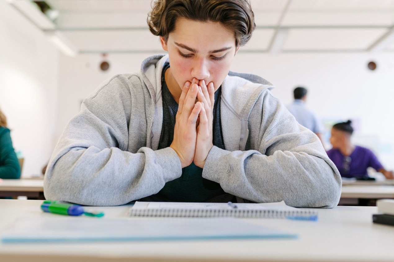 A photo shows a teenage boy in a classroom looking worriedly down at classwork on his desk.