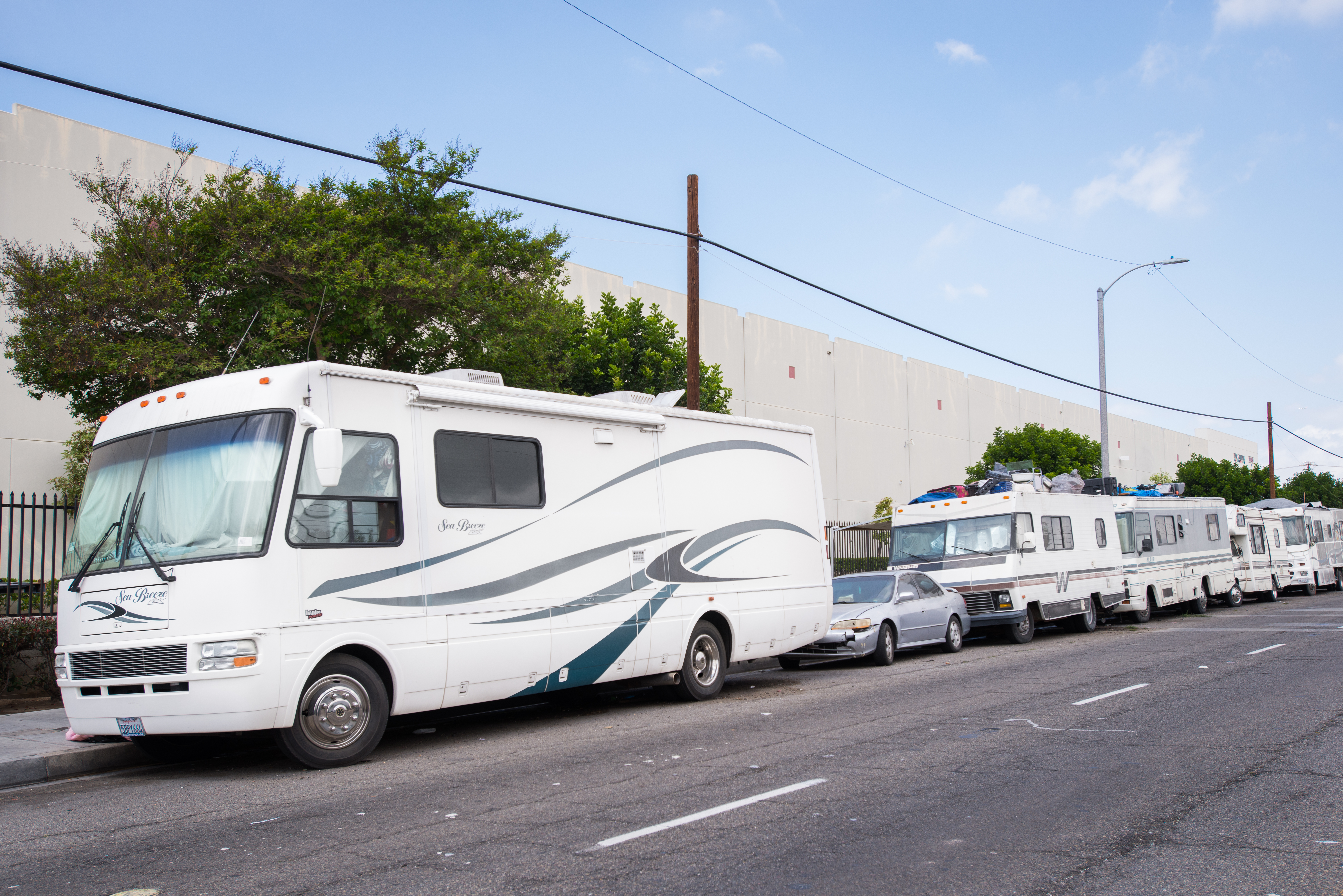 A photo shows parked RVs being used as homeless encampments along a sidewalk.