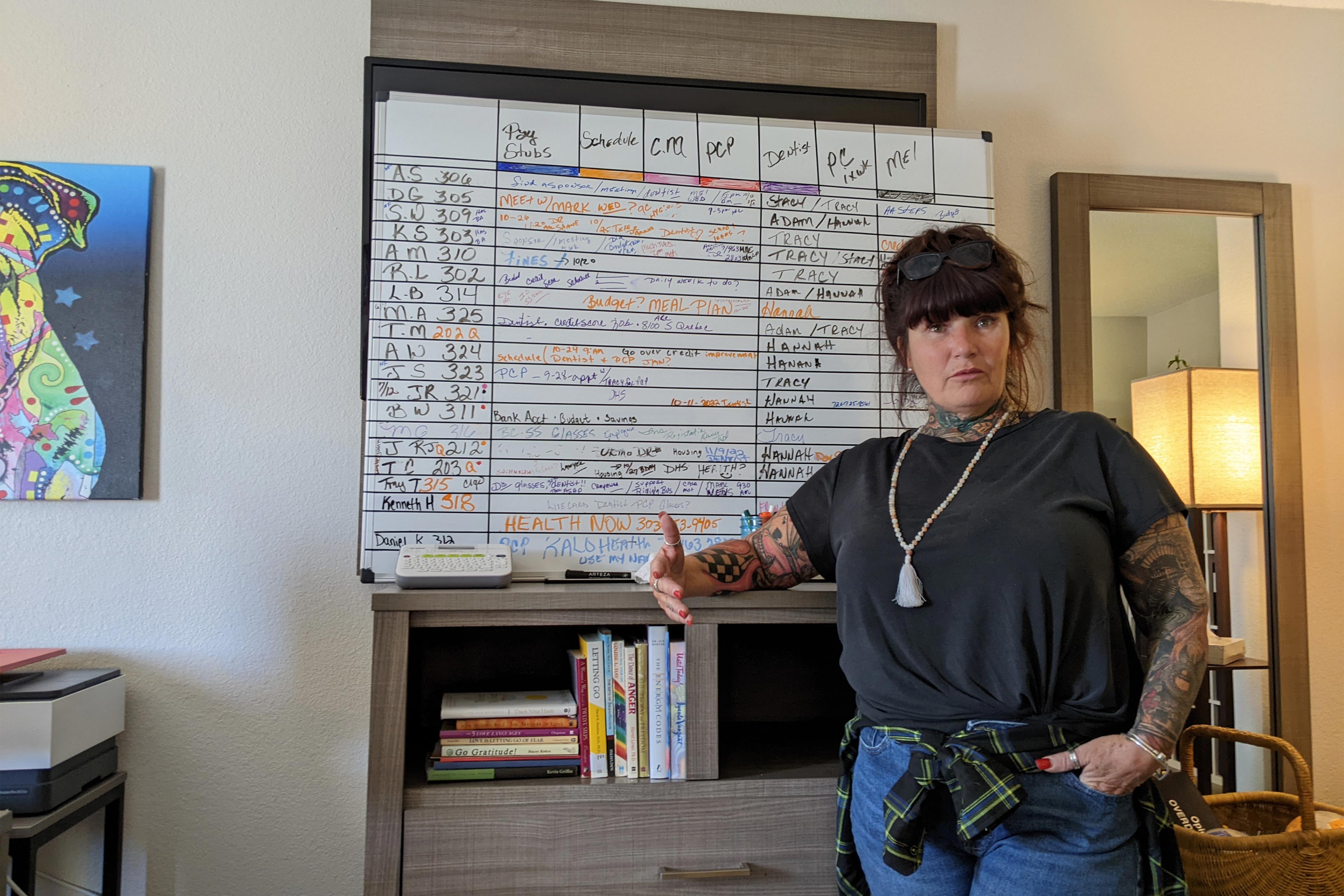 Bir fotoğrafta Donna Norton, müşterilerinin programlarını listeleyen bir beyaz tahtanın önünde duruyor.