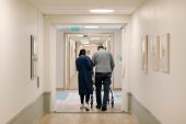 A photo shows a nurse helping an elderly patient down a hallway in a nursing home.