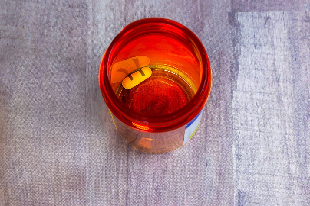 A photograph of an orange prescription bottle from above. There is only one pill left in the bottle.