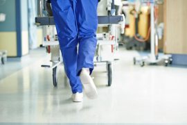 A photo shows a nurse's legs walking through a hospital corridor while pushing a gurney.