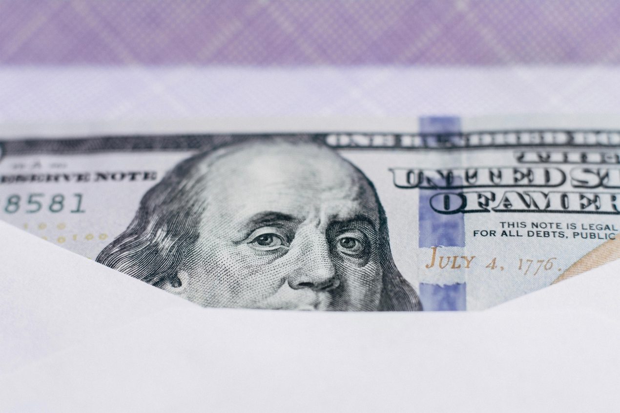 A close up photo shows a hundred dollar bill inside an envelope.