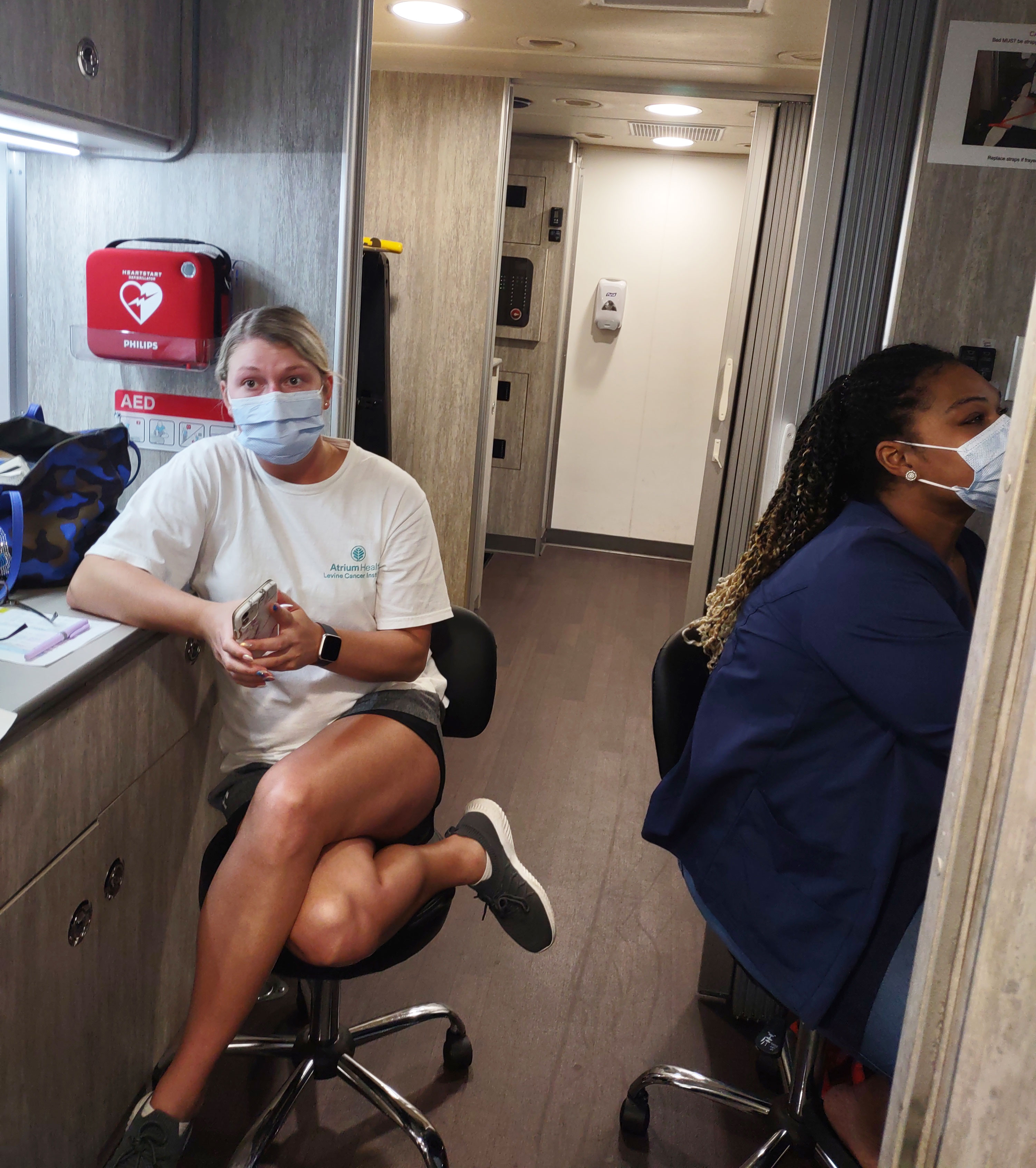 A photo shows two women sitting on stools inside of a medical bus.