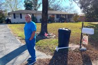 A man stands at the end of a driveway near a mailbox.