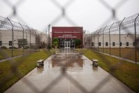 A photo shows the front entrance of Stewart Detention Center through a chain-link gate.