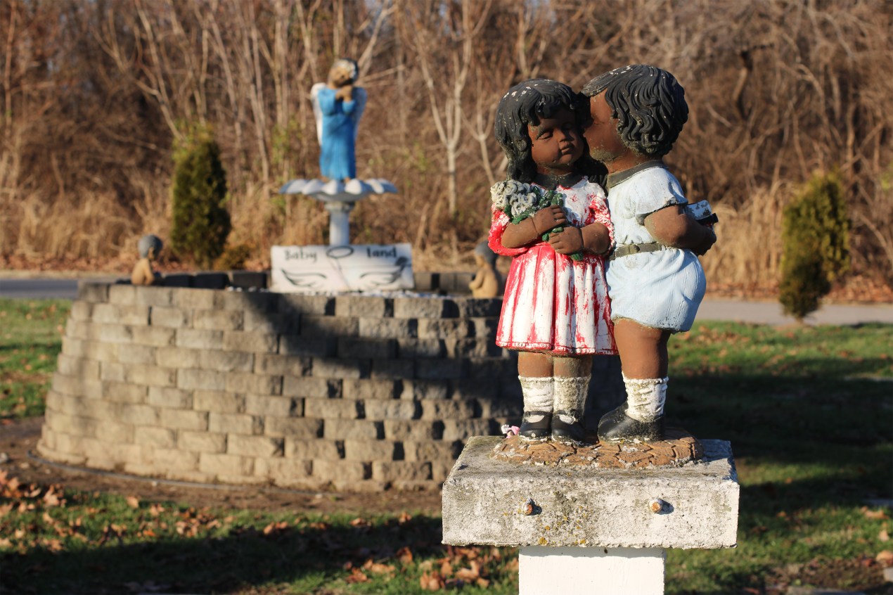 A photo shows statues of Black angels, depicted as children, in a cemetery garden.