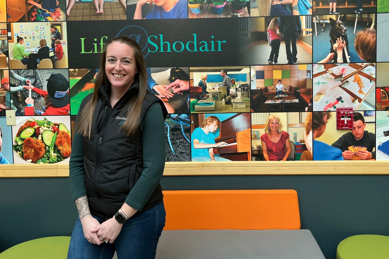 A photo shows Jenna Eisenhart posing for a portrait in front of a mural on the wall in Shodair Children's Hospital.