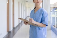 A photo shows a hospital worker standing in a hallway, holding a clipboard.