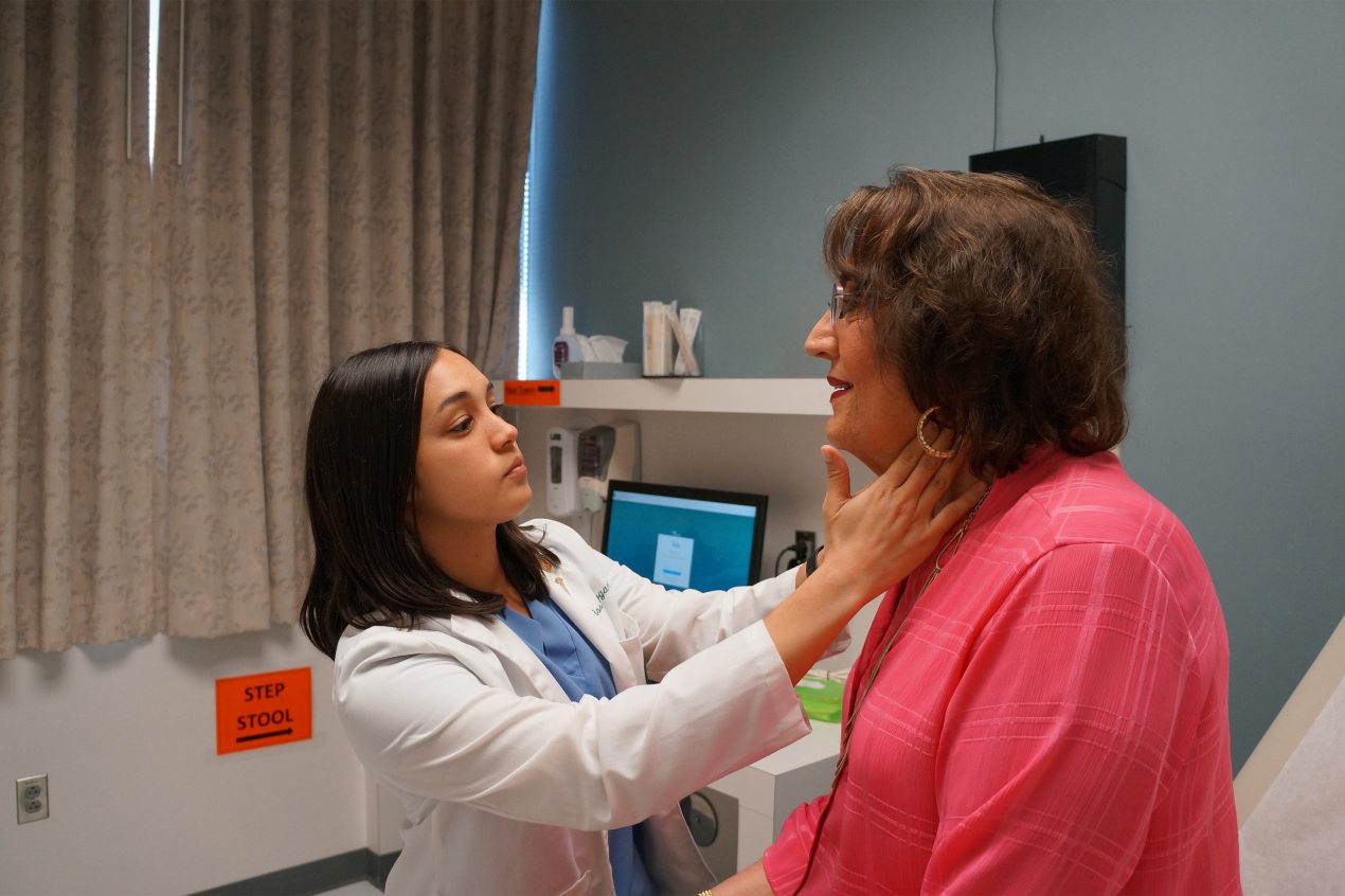 A photo shows a medical student examining a transgender woman's neck.